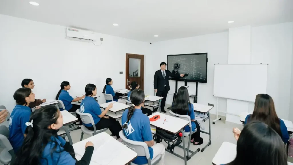 A teacher in a suit explains math on a blackboard to attentive students in blue uniforms. The classroom is modern, bright, and focused.